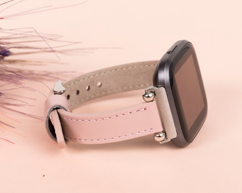 May include: A pink leather watch band with silver accents and a black smartwatch face.