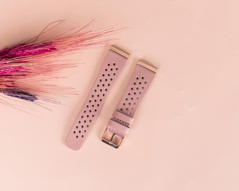 Puede incluir: Dos correas de reloj de color rosa claro con un dise&ntilde;o perforado y herrajes dorados.