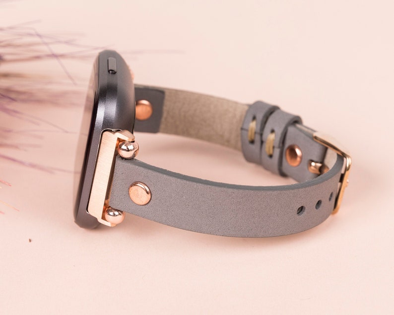 May include: A gray leather watch band with rose gold hardware and a black watch face.