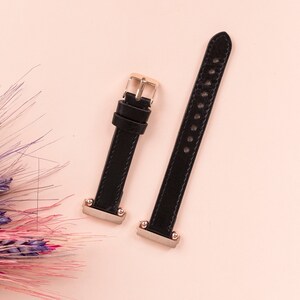 May include: Two black leather watch straps with gold accents. The straps have multiple holes for adjusting the size.