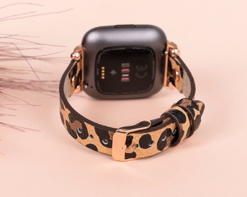 May include: A brown and black leopard print watch band with a rose gold buckle and a black smartwatch face.