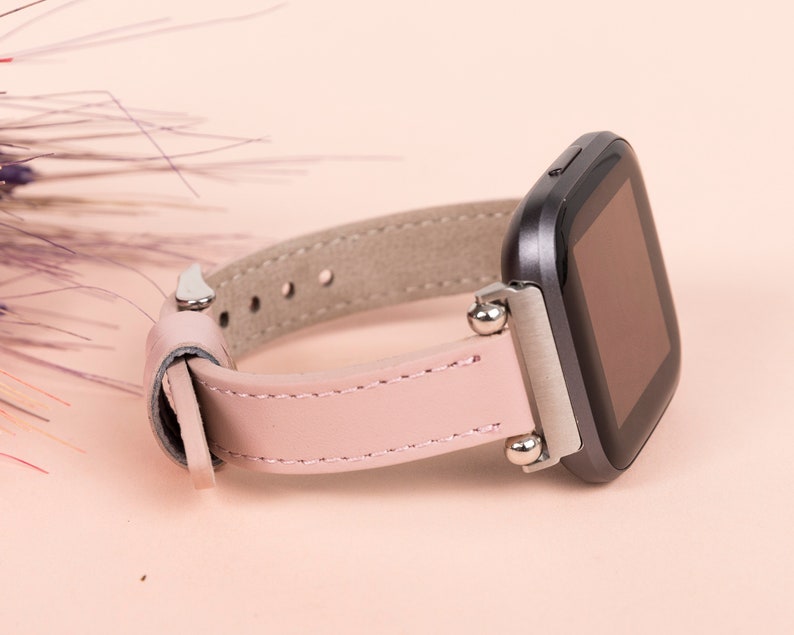 May include: A pink leather watch band with silver accents and a black smartwatch face.