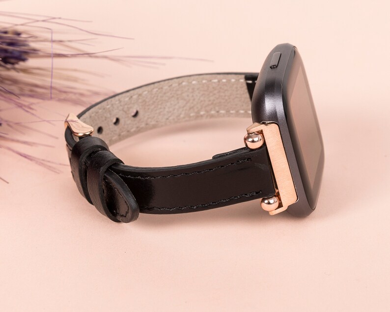 May include: A black leather watch strap with rose gold accents and a black square watch face.