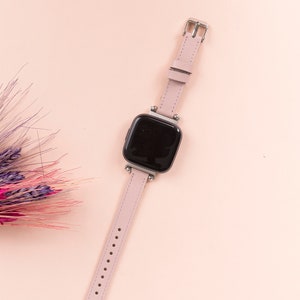 May include: A pink leather watch band with a black square watch face. The watch is on a pink background.