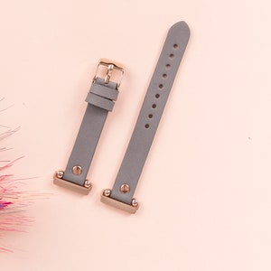 May include: Two gray leather watch bands with rose gold hardware. The bands are flat and have a smooth finish. The hardware includes a buckle and two small studs.
