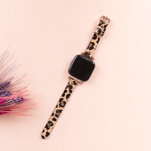 May include: A black and brown leopard print watch band with a black watch face. The band has gold accents and is on a pink background.