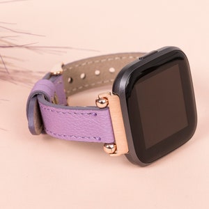 May include: A purple leather watch band with rose gold accents and a black smartwatch face.