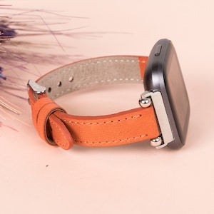 May include: A brown leather watch strap with silver metal clasps and a black smartwatch.
