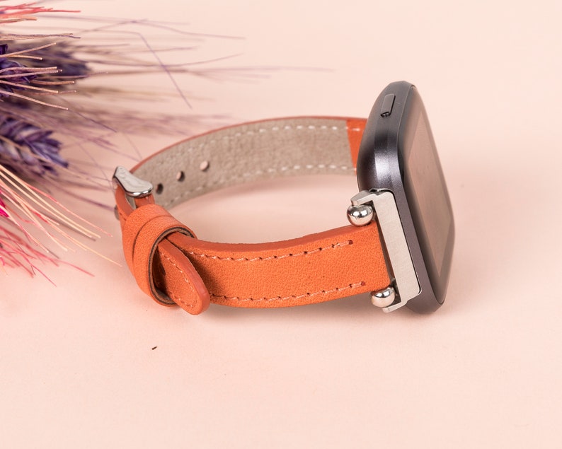 May include: A brown leather watch strap with silver metal clasps and a black smartwatch.