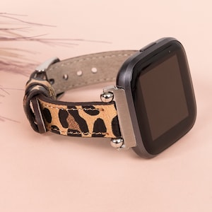 K&ouml;nnte beinhalten: Eine schwarze Smartwatch mit einem Armband aus Leder im Leopardenmuster. Das Zifferblatt der Uhr ist schwarz und das Armband hat silberne Akzente.