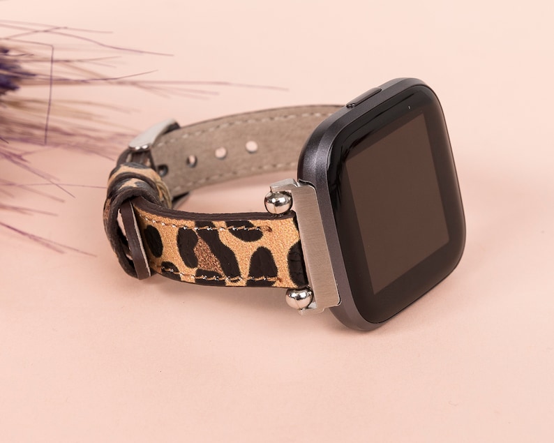 K&ouml;nnte beinhalten: Eine schwarze Smartwatch mit einem Armband aus Leder im Leopardenmuster. Das Zifferblatt der Uhr ist schwarz und das Armband hat silberne Akzente.