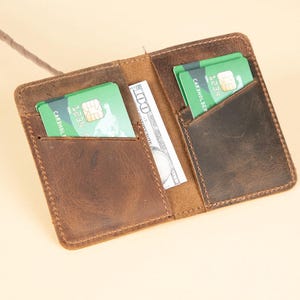 Peut inclure: Un portefeuille en cuir marron avec deux emplacements pour cartes et un porte-billets. Le portefeuille a un aspect vieilli et est ouvert pour montrer l'int&eacute;rieur.