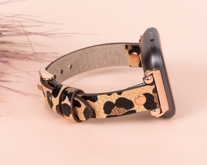 May include: A leopard print watch band with rose gold accents. The band is made of leather and has a buckle closure.