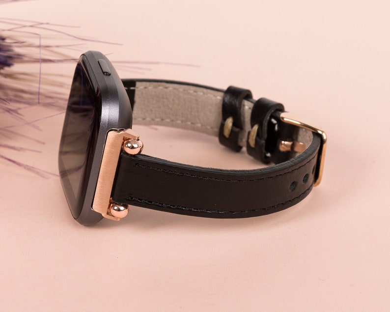 May include: A black leather watch strap with rose gold accents and a square-shaped watch face.