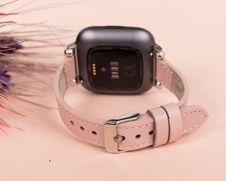 May include: A pink leather watch band with a silver buckle and a black watch face. The watch face has a small screen and the text "CE" on it.