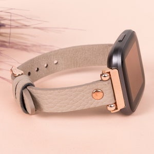 May include: A gray leather watch band with rose gold accents and a black square watch face.