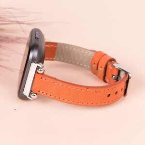 May include: A close-up of a brown leather watch strap with silver hardware. The strap is attached to a black smartwatch.