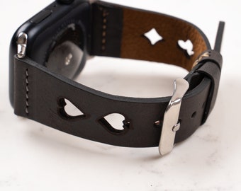 May include: A black smartwatch with a dark brown leather band featuring cut-out heart and diamond shapes. The band includes a silver-toned metal buckle and visible stitching along the edges, attached to a black watch casing.