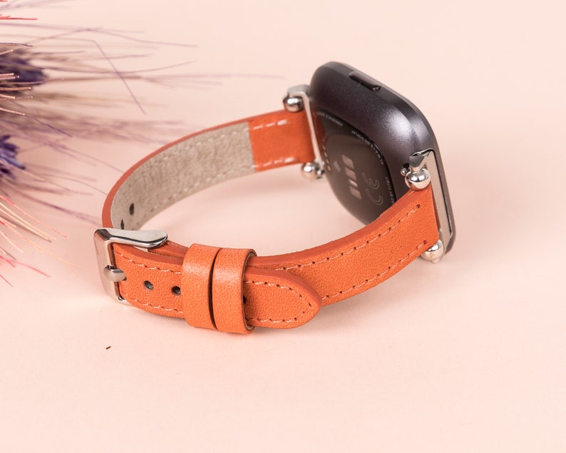 May include: Orange leather band with silver accents for a smartwatch. The band is made of genuine leather and has a classic look.