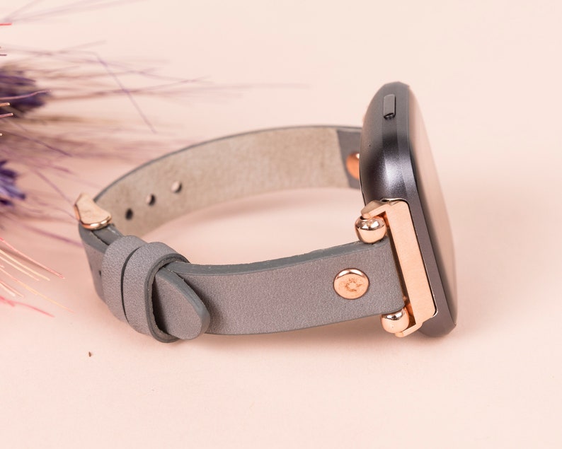 May include: A gray leather watch band with rose gold accents and a black square watch face.