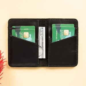 Peut inclure: Portefeuille en cuir noir avec deux emplacements pour cartes et une poche pour l'argent. Le portefeuille est ouvert et contient deux cartes de cr&eacute;dit et un billet d'un dollar.