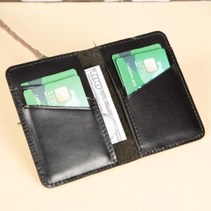 Peut inclure: Un portefeuille en cuir noir avec deux emplacements pour cartes et un porte-billets. Le portefeuille est ouvert et contient deux cartes de cr&eacute;dit et un billet de dollar.