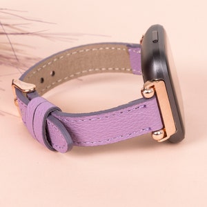 May include: A purple leather watch band with rose gold accents and a black watch face.