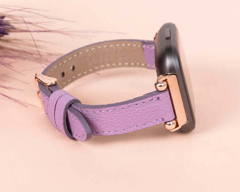 May include: A purple leather watch band with rose gold accents and a black watch face.