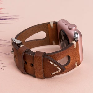 May include: A brown leather watch band with white stitching and a rose gold Apple Watch.