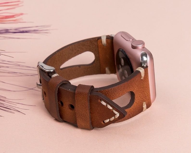 May include: A brown leather watch band with white stitching and a rose gold Apple Watch.