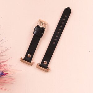 May include: A black watch strap consisting of two separate pieces with rose gold hardware. The strap features a rose gold buckle, two matching loops, and rose gold metal connectors at the ends. The leather-like material has a smooth finish.