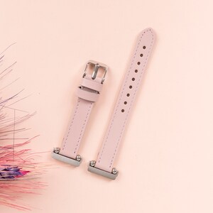 May include: Two pink leather watch bands with silver buckles. The bands are laid out on a pink background.