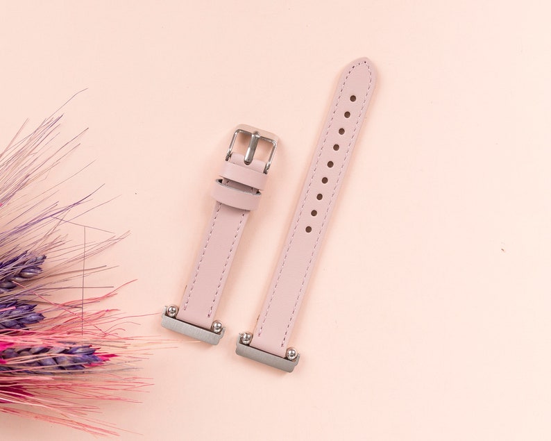 May include: Two pink leather watch bands with silver buckles. The bands are laid out on a pink background.