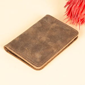 Peut inclure: Un portefeuille en cuir marron avec une finition vieillie. Le portefeuille est ferm&eacute; et a un bord cousu.