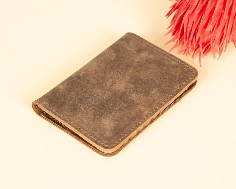Peut inclure: Un portefeuille en cuir marron avec une finition vieillie. Le portefeuille est ferm&eacute; et a un bord cousu.