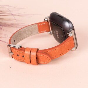 May include: A brown leather watch strap with silver accents and a black smartwatch face. The strap has a buckle fastening.