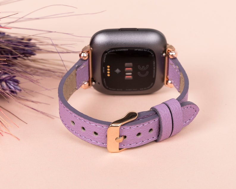 May include: A lavender leather watch band with rose gold hardware. The band is designed for a smartwatch with a square face.