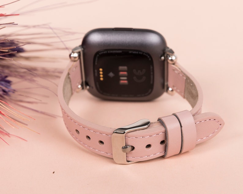 May include: A pink leather watch band with a silver buckle and a black watch face. The watch face has a small screen and the text "CE" on it.
