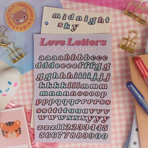 Op de afbeelding: Een vel met pastelroze, blauwe en groene letter stickers met de woorden "Love Letters" en "Tiny Taro Studios" bovenaan gedrukt. De stickers tonen de letters van het alfabet in een vet, afgerond lettertype.