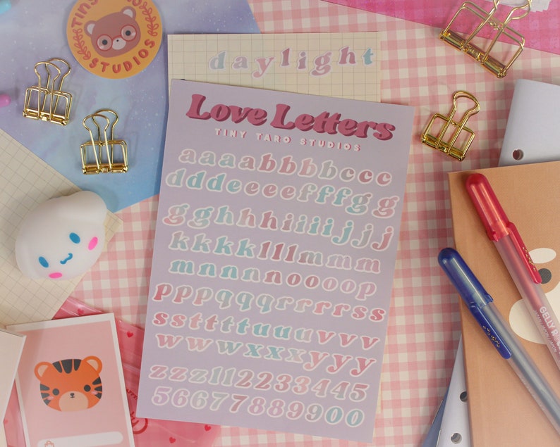 Op de afbeelding: Een vel met pastelkleurige alfabetstickers met de woorden "Love Letters" en "Tiny Taro Studios" erop gedrukt. De letters zijn in een retro, afgerond lettertype.