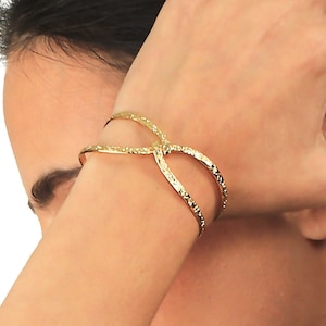 Puede incluir: Un brazalete de oro cruzado con acabado texturizado.