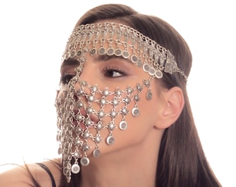May include: A woman wearing a silver chainmail face mask with coin accents. The mask is attached to a headband and covers the forehead, eyes, nose, and mouth. The woman is wearing a black tank top.