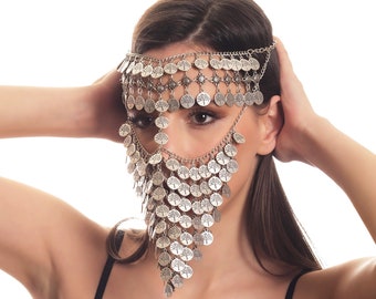 May include: A woman wearing a black tank top with a silver coin chain headpiece. The headpiece is made of many small coins with a tree design.