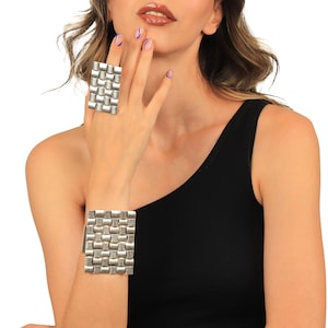 May include: A silver bracelet and ring with a geometric design. The bracelet is wide and has a square shape. The ring is smaller and also has a square shape.