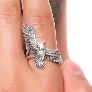 Puede incluir: Un anillo de plata con un diseño de águila detallado. El águila tiene las alas extendidas y mira hacia la derecha.