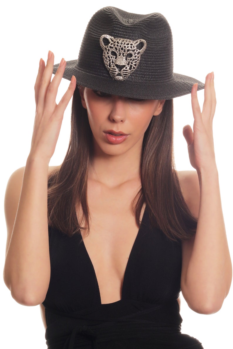 Puede incluir: Una mujer con un sombrero negro con un dise&ntilde;o de leopardo enjoyado y un top negro de cuello en V.