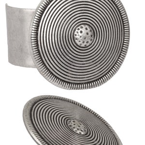 May include: A silver cuff bracelet with a large, round, concentric circle design. The center of the circle has a textured, raised design.