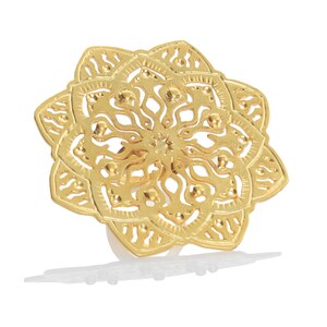 May include: A gold-colored ring with a detailed mandala design. The ring is made of metal and has a delicate, intricate pattern.