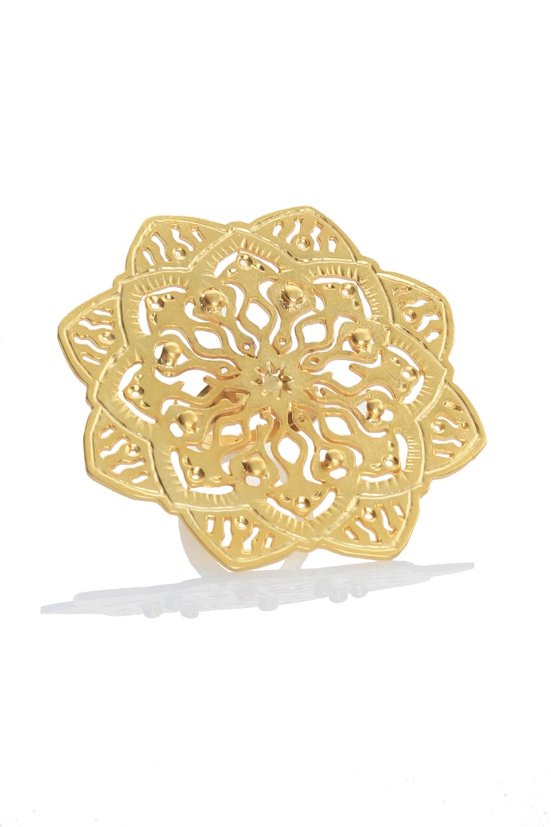 May include: A gold-colored ring with a detailed mandala design. The ring is made of metal and has a delicate, intricate pattern.