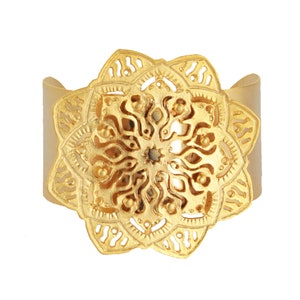 May include: Gold-toned metal cuff bracelet with a large, ornate, circular mandala design.